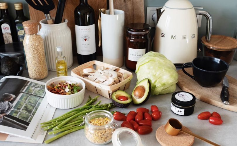 Assorted healthy food and vegetables set locating on gray countertop next to various utensils and appliances during cooking in stylish kitchen