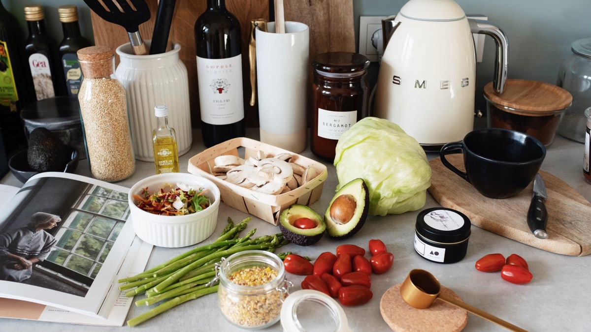 Assorted healthy food and vegetables set locating on gray countertop next to various utensils and appliances during cooking in stylish kitchen